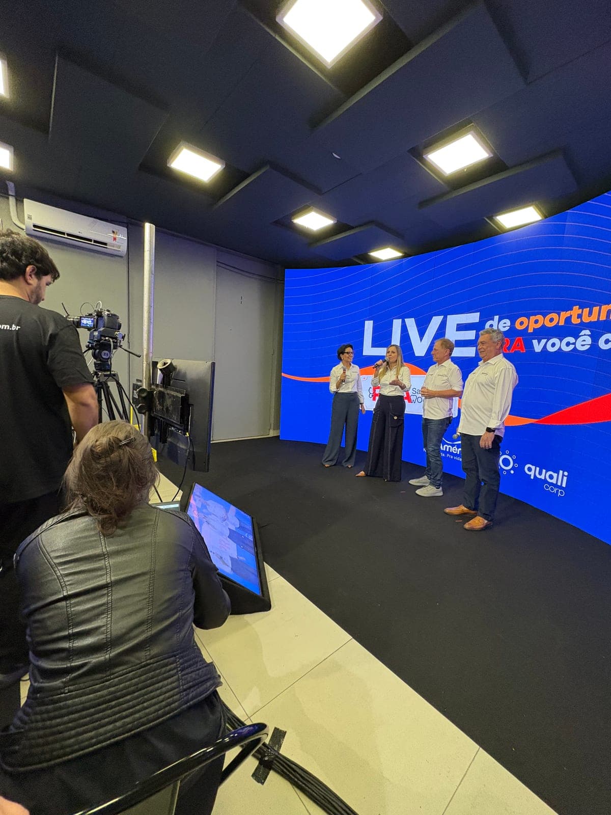 Câmera em primeiro plano, com o monitor exibindo o enquadramento da gravação, diante do painel de LED curvo do estúdio com o cenário montado