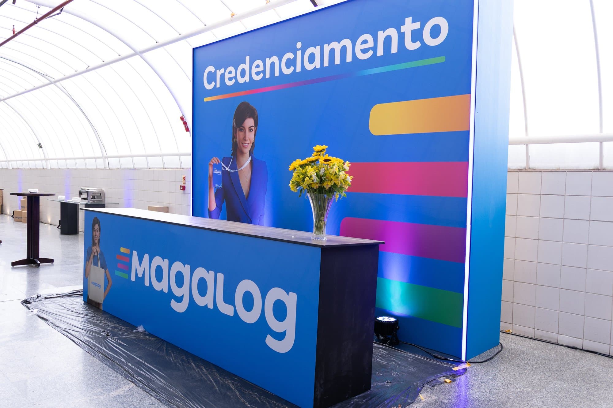 Balcão de credenciamento com a marca do evento e painel de fundo com a palavra credenciamento na identidade visual