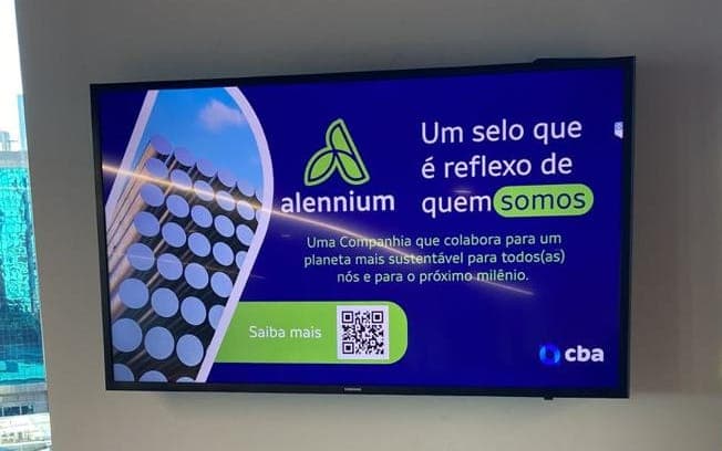 Tela corporativa instalada em área de circulação de escritório, exibindo uma campanha institucional