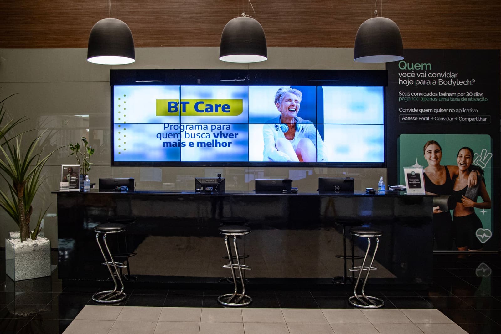 Videowall atrás do balcão de recepção de uma academia Bodytech, exibindo uma campanha em tela única